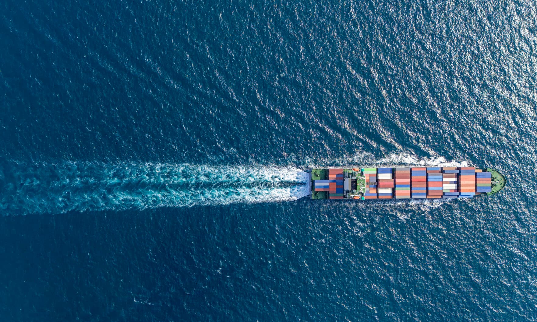 Aerial top view container ship full speed with beautiful wave pattern at blue sea.